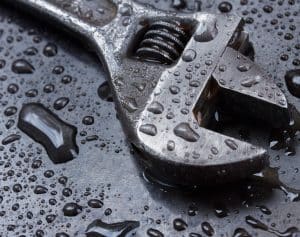 A close-up of a metal adjustable wrench lying on a wet, dark surface, covered in water droplets. | High 5 Plumbing, Heating & Cooling