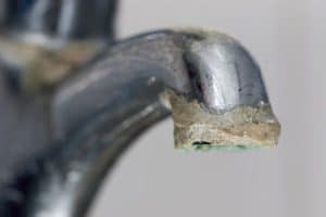 A close-up of a metal faucet with a significant buildup of white and brown limescale deposits around the spout highlights the importance of limescale prevention in the home. | High 5 Plumbing, Heating & Cooling