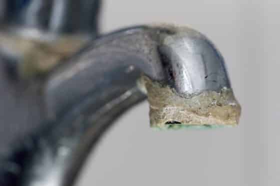 A close-up of a metal faucet with a significant buildup of white and brown limescale deposits around the spout highlights the importance of limescale prevention in the home. | High 5 Plumbing, Heating & Cooling