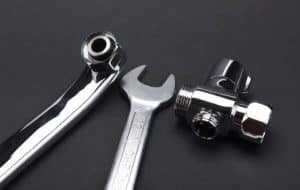 A close-up of a chrome-plated wrench and two metal plumbing fittings on a plain black background, highlighting essential tools used to fix frozen pipes and prevent frozen pipes during winter. | High 5 Plumbing, Heating & Cooling