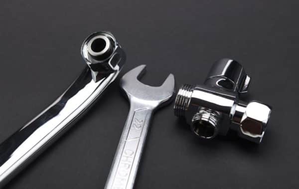 A close-up of a chrome-plated wrench and two metal plumbing fittings on a plain black background, highlighting essential tools used to fix frozen pipes and prevent frozen pipes during winter. | High 5 Plumbing, Heating & Cooling