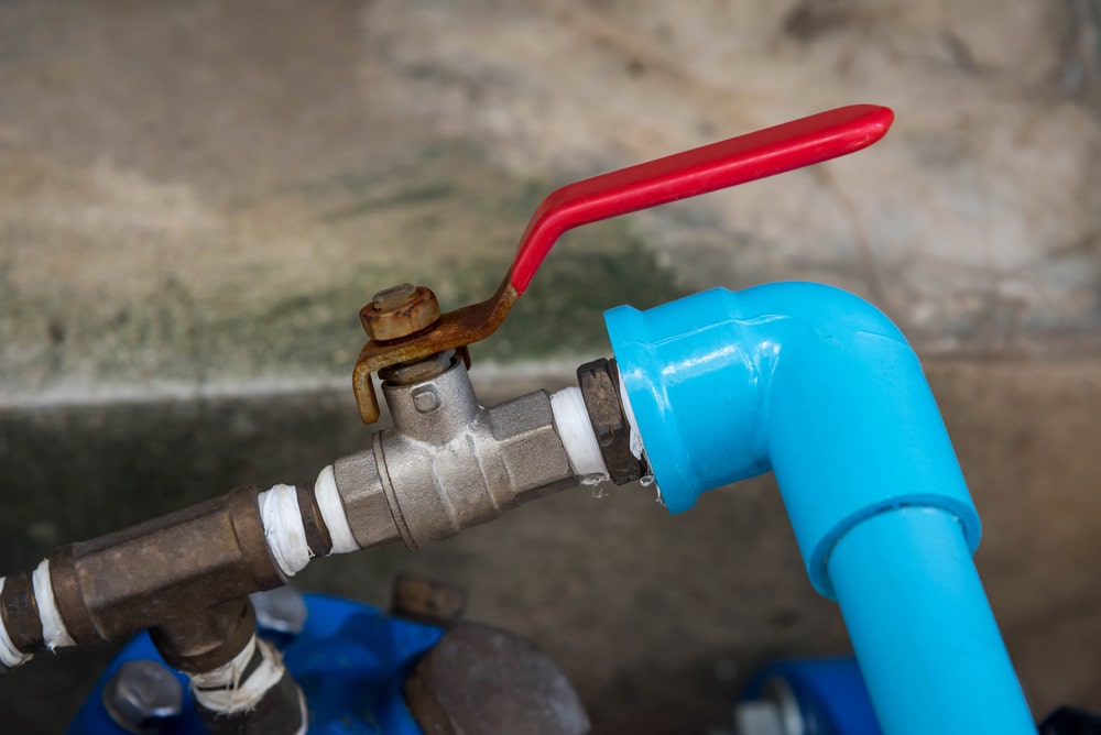 Close-up of a metal water shut-off valve with a red lever handle connected to a blue PVC pipe at a right angle, with a small water leak visible at the joint—an essential detail for any shut-off valve guide. | High 5 Plumbing, Heating & Cooling