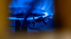 A close-up view of a lit blue gas flame on a stovetop burner, with an igniter and wires visible in the foreground, highlights the pilot light importance for safely igniting and maintaining the burner flame. | High 5 Plumbing, Heating & Cooling