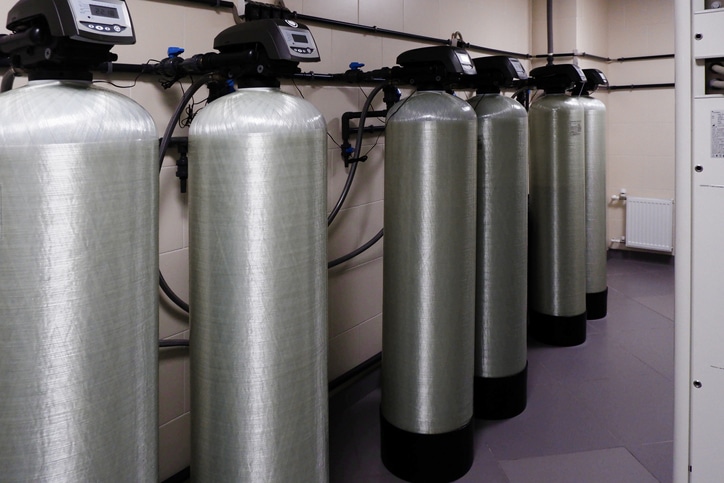 Water softener tanks with control valves installed in a treatment room.