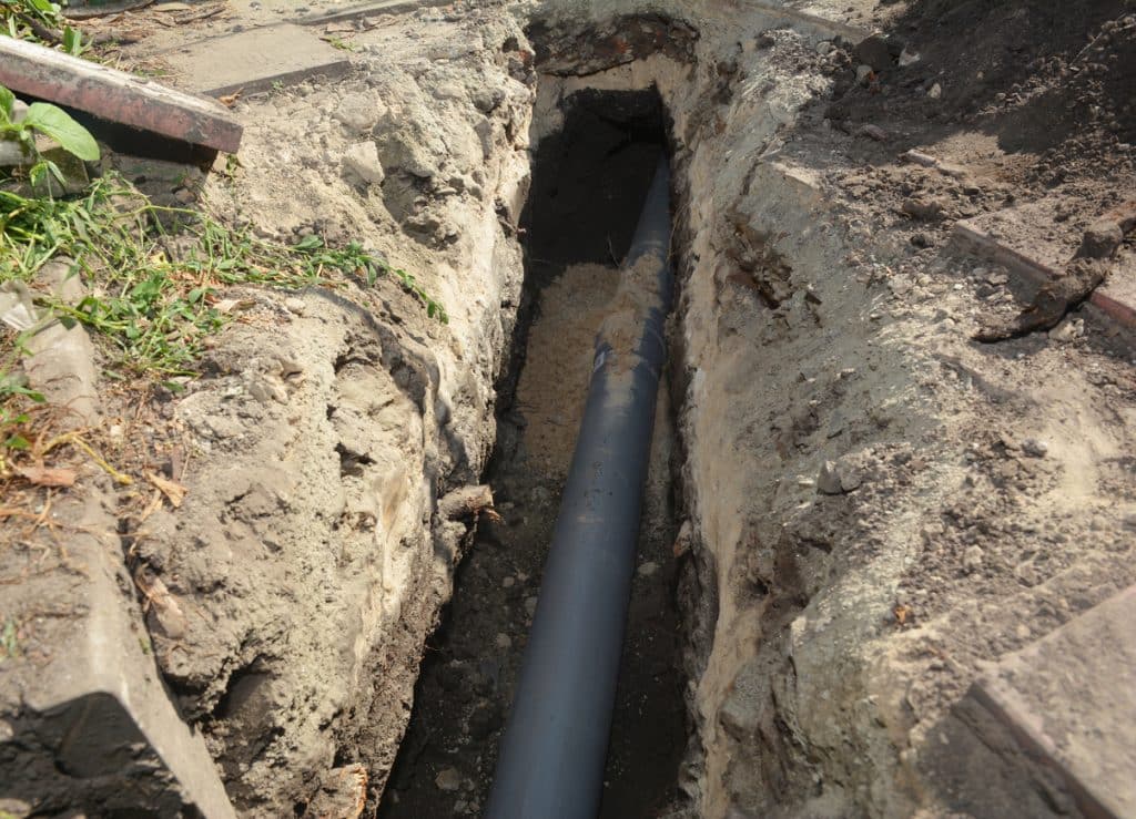 Black sewer pipe installed in a trench surrounded by exposed soil and concrete, showing an underground drainage line during construction.